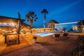 A poolside area with a bar, lounge chairs, and a thatched-roof structure.