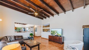 A spacious living room with a sofa, coffee table, and TV, a dining area with a table and chairs, and a kitchen visible through an open door. - Villa Rancho Azul Mins to Palm Beach & Eagle Beach (Noord)