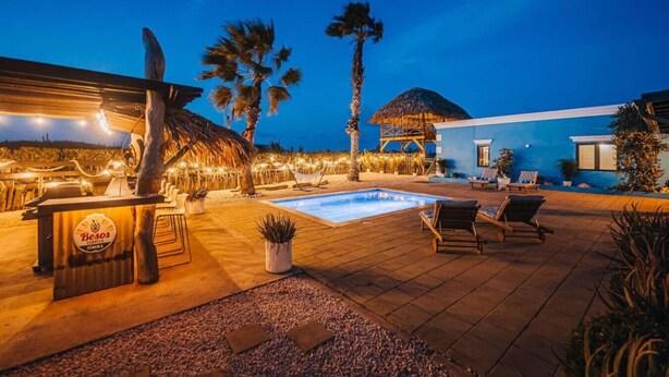 A poolside area with a bar, lounge chairs, and a thatched-roof structure. - Villa Rancho Azul Mins to Palm Beach & Eagle Beach (Noord)