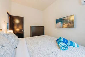 A hotel room with a bed, a dark wooden wardrobe, a wall-mounted painting, and a lamp.