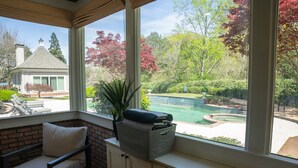 A sunlit room with a view of a swimming pool and a brick wall.