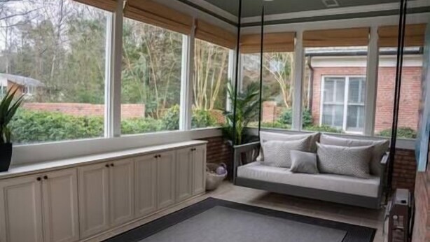 A sunroom with a built-in swing chair, large windows, and a view of the outdoors.