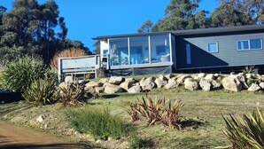 A modern house with a glass extension, surrounded by a natural landscape with rocks and native plants. - Private Two Bedroom unit located on 63 acres Stunning views. 
Beautiful Sunroom. (Mountain River)