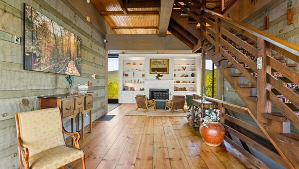 Een ruime kamer met houten vloeren, een open haard en een verzameling boeken en decoratieve objecten op planken.