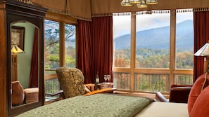 A bedroom with a large window, a bed, a chair, and a table with a bottle and glasses.