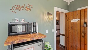 A kitchenette with a microwave, coffee maker, and a coffee-themed wall decal. - Stunning View | Walk-In Shower | Balcony + TV Seating (Townsend)