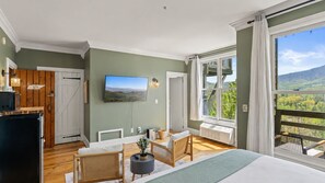 Ein Zimmer mit Bett, Fernseher, Esstisch und einem Balkon mit Blick.