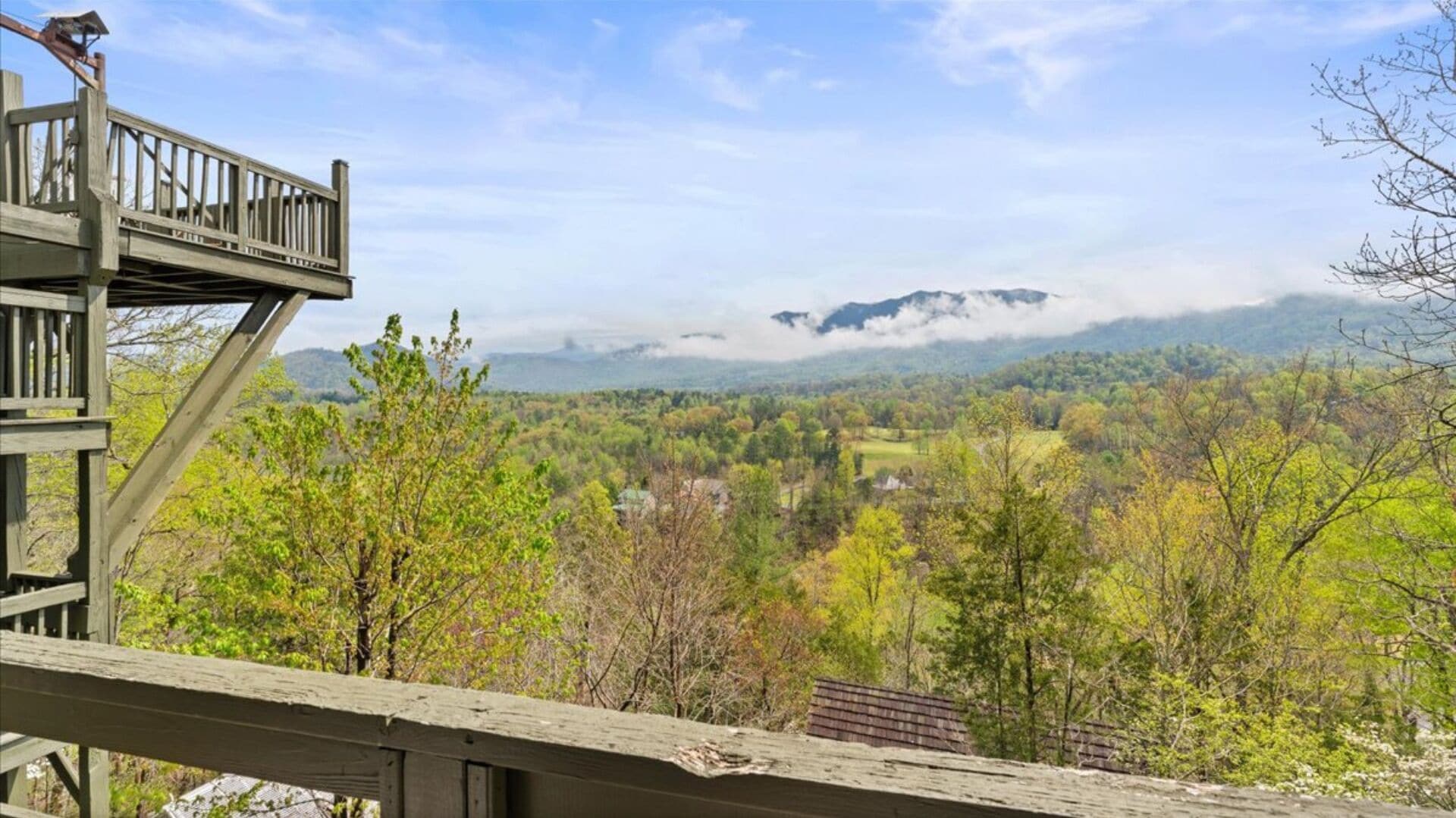 A wooden observation deck overlooking a valley with trees and distant mountains.