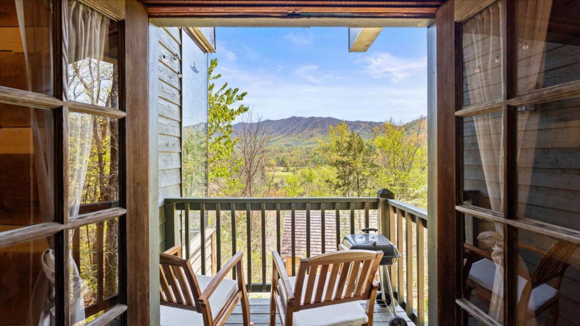 An open balcony with wooden chairs and a grill, overlooking a mountainous landscape.