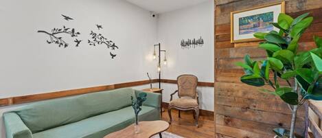 Ein Zimmer mit einem grünen Sofa, einem Holzstuhl, einem kleinen Tisch, einer Wandleuchte und einem gerahmten Bild.
