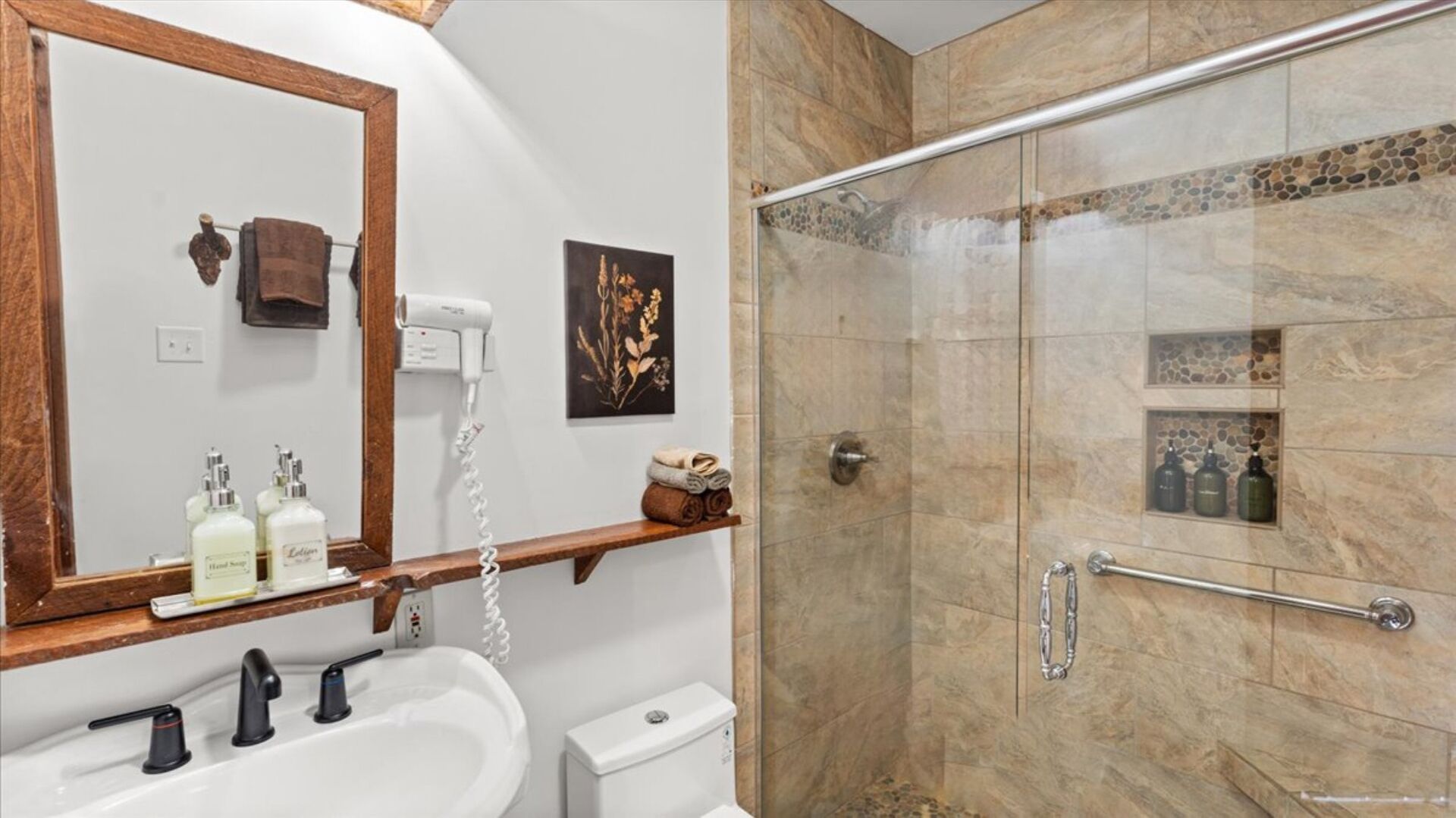 A bathroom with a sink, mirror, hairdryer, and toiletries.