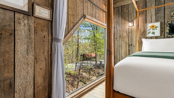 A wooden cabin room with a bed, a window, and a framed picture on the wall.