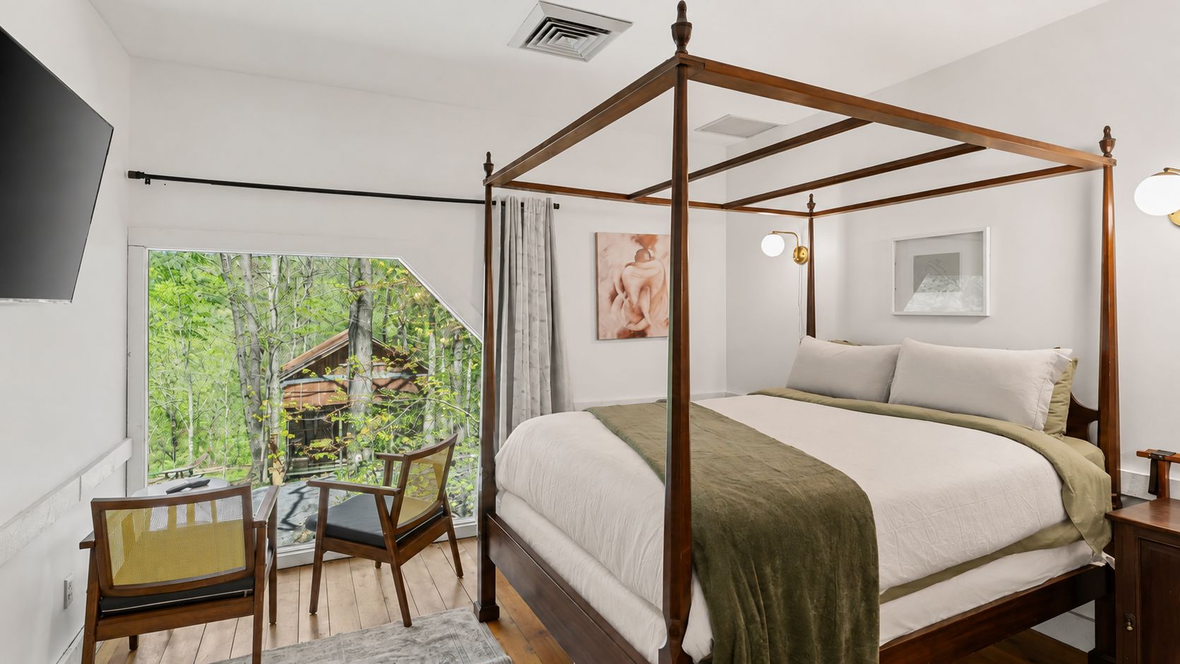 Una cama con dosel con vistas a un bosque a través de un ventanal grande.