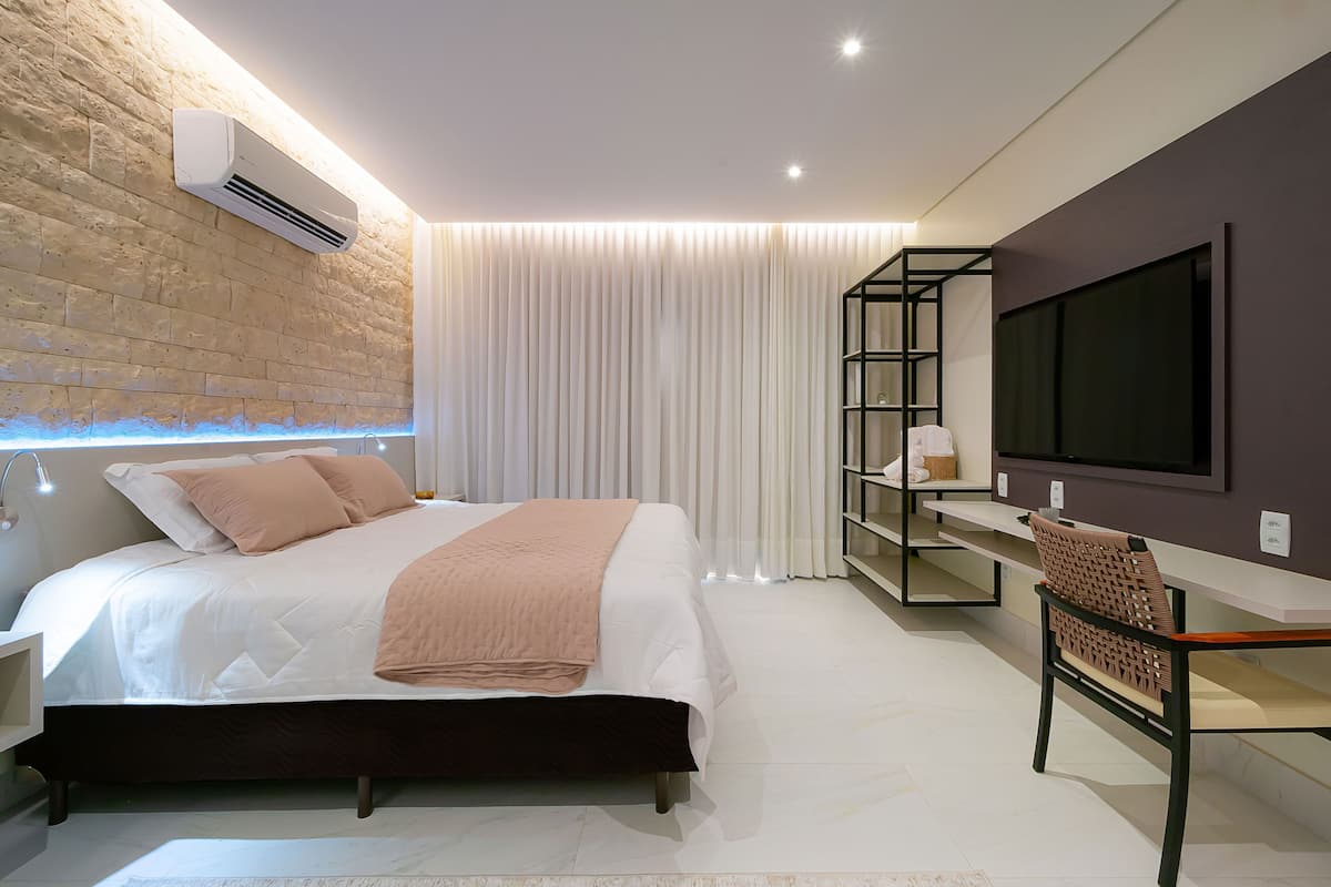 Une chambre à coucher moderne avec un grand lit, un téléviseur fixé au mur, un bureau avec une chaise et une bibliothèque.