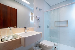 A modern bathroom with a glass shower enclosure, a white sink, and a wooden vanity. - Joia Rara Pousada (Pirenópolis)