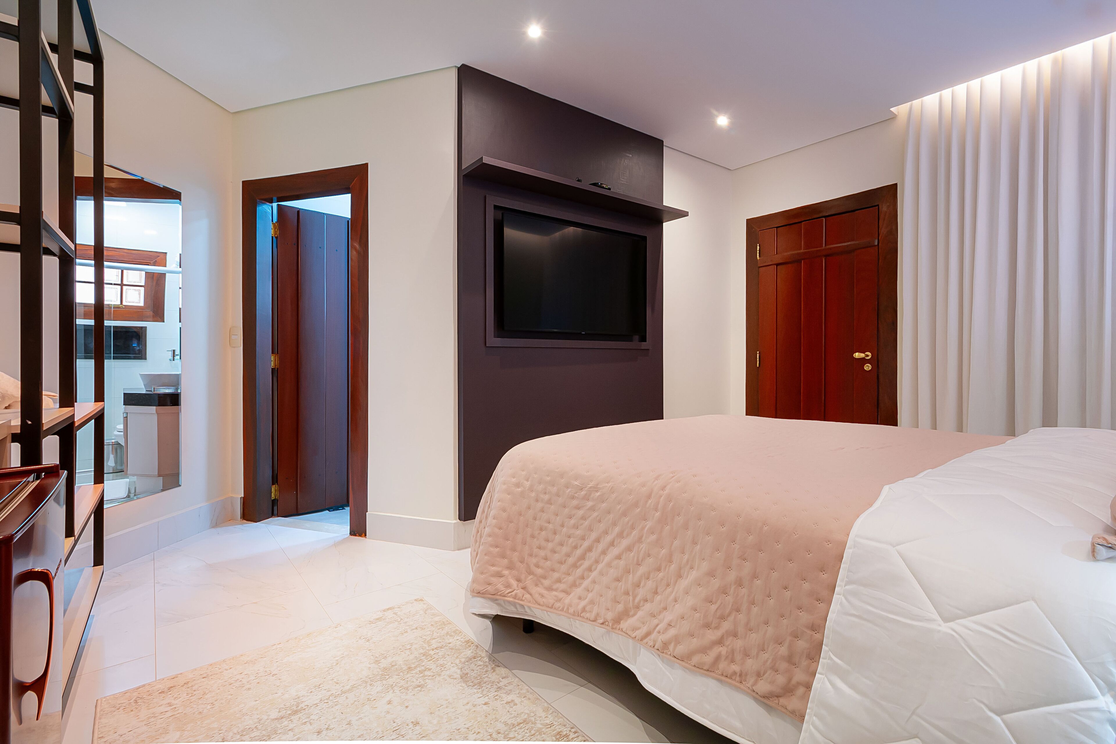 Une chambre moderne avec un grand lit, un téléviseur à écran plat fixé au mur et une armoire en bois.