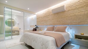 A modern bedroom with a large bed, a glass shower enclosure, and a brick accent wall. - Joia Rara Pousada (Pirenópolis)