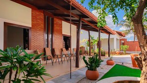 A covered outdoor seating area with wicker chairs, a brick wall, and potted plants. - Joia Rara Pousada (Pirenópolis)