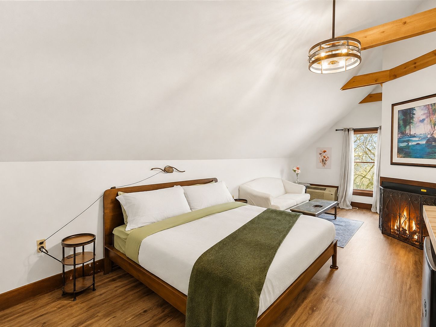 A bedroom with a wooden bed, a bedside table, a lamp, a chair, a fireplace, and a painting on the wall.