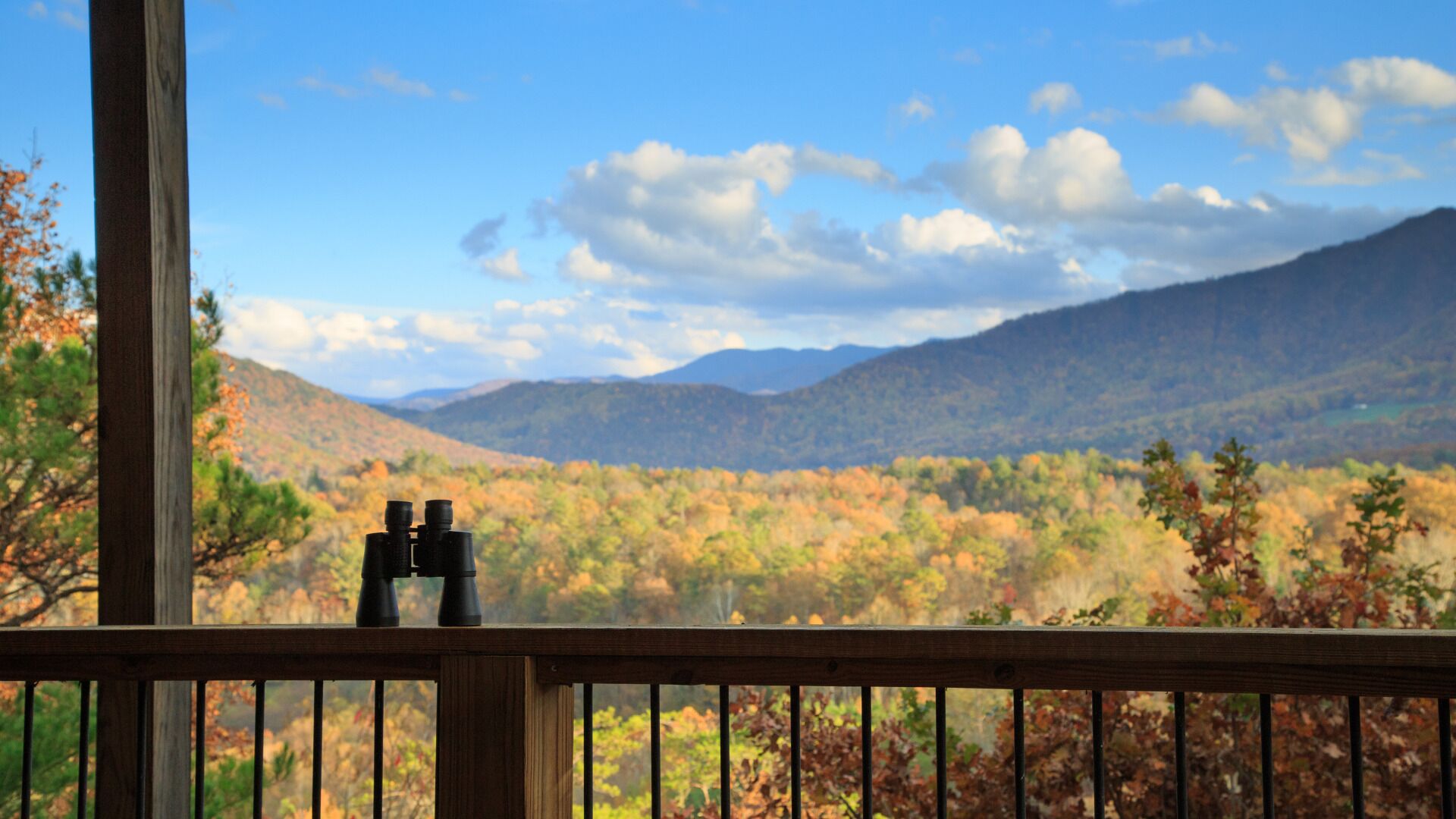 A wooden deck with binoculars on it, overlooking a mountainous landscape with autumn foliage.
