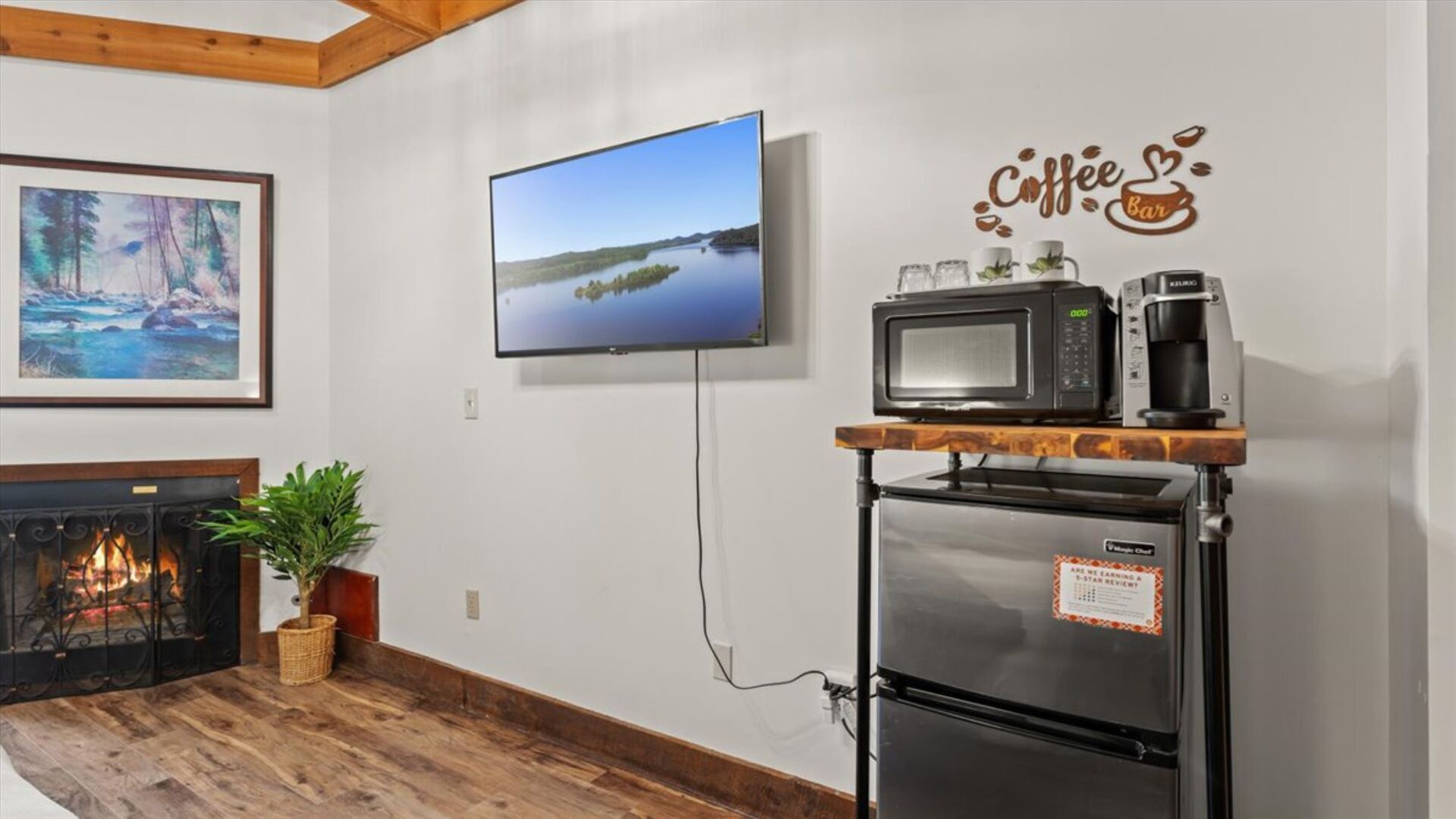 A living room with a fireplace, a flat-screen TV, a coffee station, and a painting.