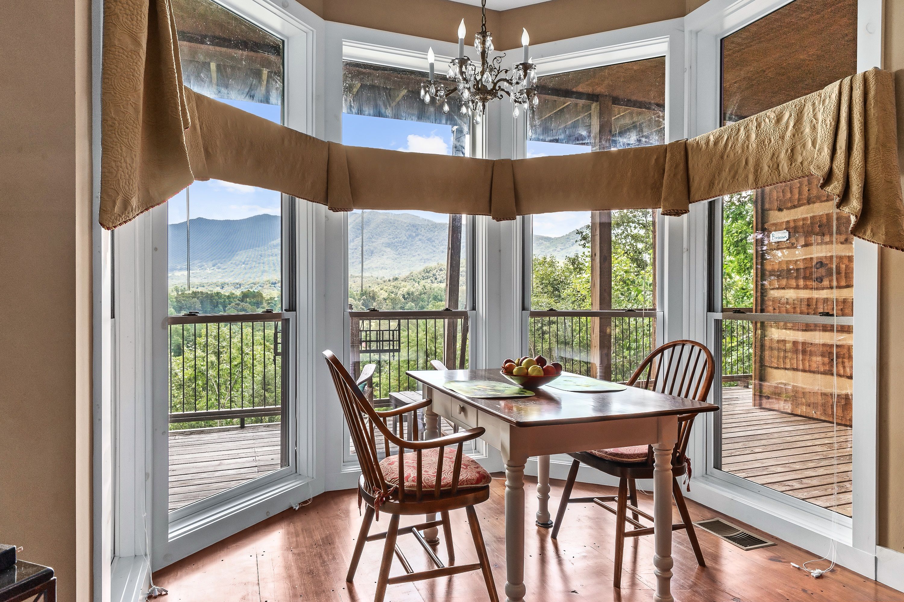 Un comedor con una mesa y sillas, una araña de cristal y ventanas amplias con vistas al exterior.