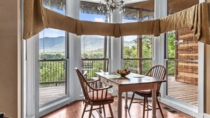 A dining area with a table and chairs, a chandelier, and large windows with a view of the outdoors.