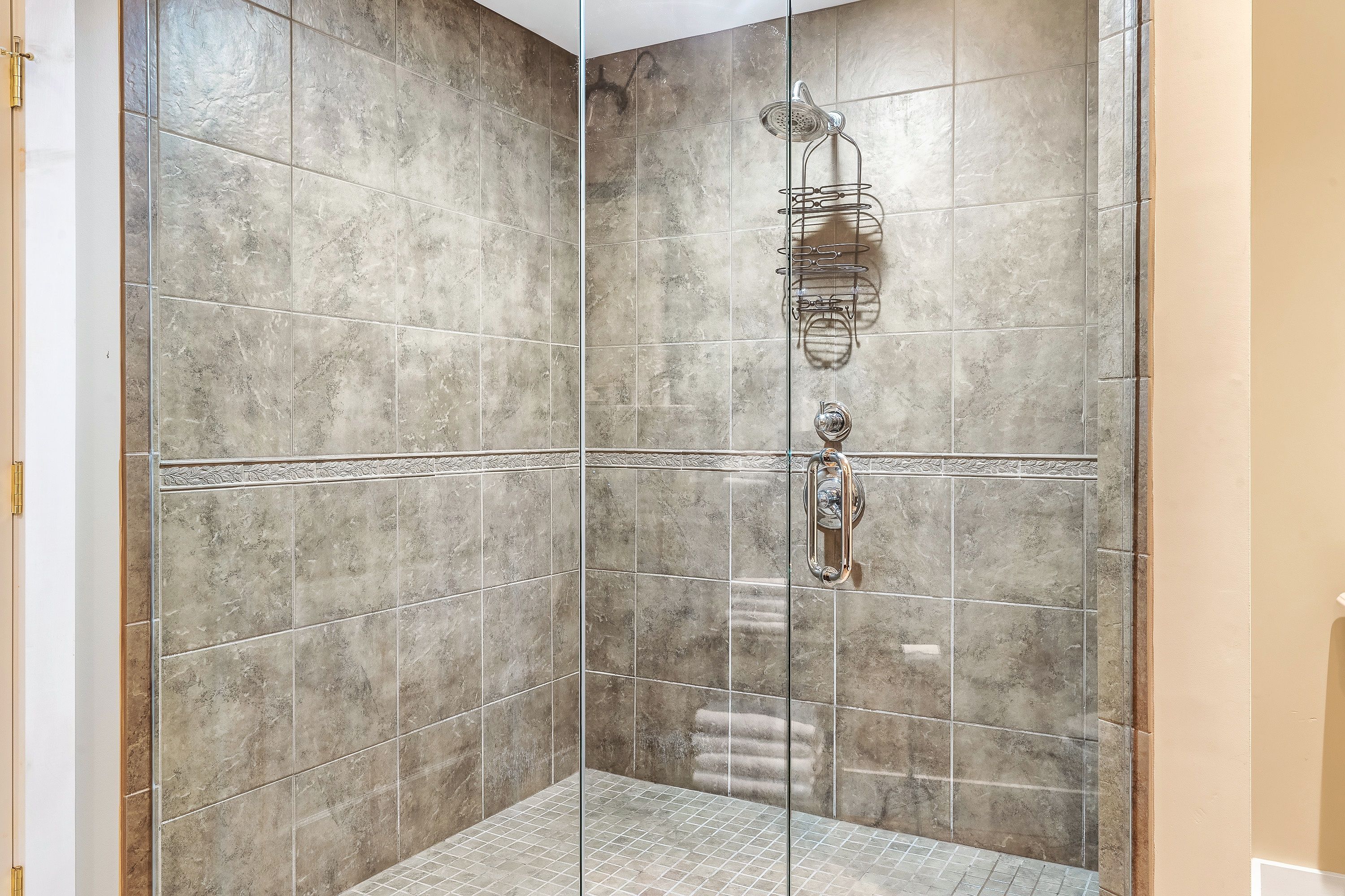 Una ducha a ras de suelo con mampara de vidrio, paredes con azulejos y un cabezal de ducha en la pared.