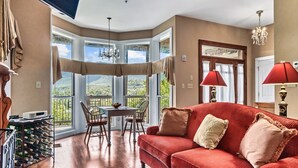 A spacious living room with a red sofa, a dining table with chairs, and a view of the outdoors through large windows.
