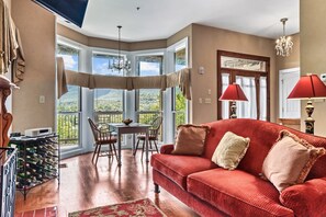 A spacious living room with a red sofa, a dining table with chairs, and a view of the outdoors through large windows. - Romantic Suite | Mountain Views! | King Bed (Townsend)