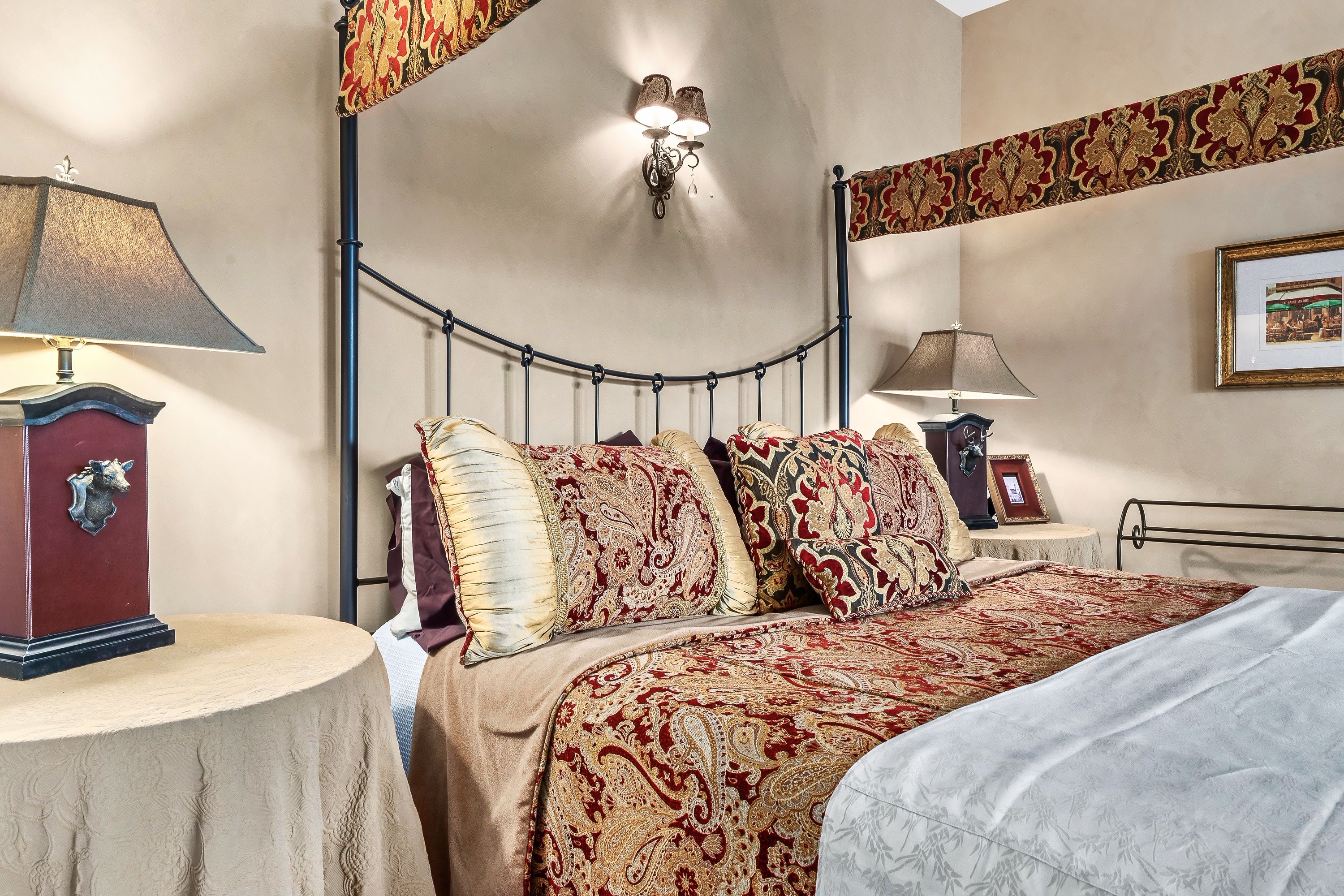 Une chambre à coucher avec un lit, deux tables de chevet, une lampe fixée au mur et un tableau encadré.