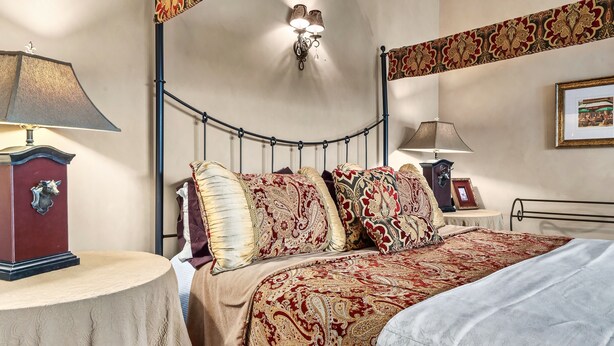 A bedroom with a bed, two bedside tables, a wall-mounted lamp, and a framed picture.