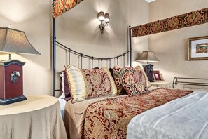 A bedroom with a bed, two bedside tables, a wall-mounted lamp, and a framed picture. - Bordeaux - Mountain View Suite with Whirlpool Tub & Fireplace (Townsend)