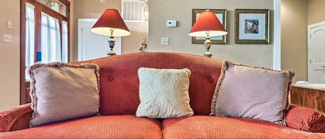 Un sofá rojo con almohadones decorativos, una araña y cuadros en la pared.