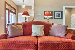 A red sofa with decorative pillows, a chandelier, and framed artwork on the wall.