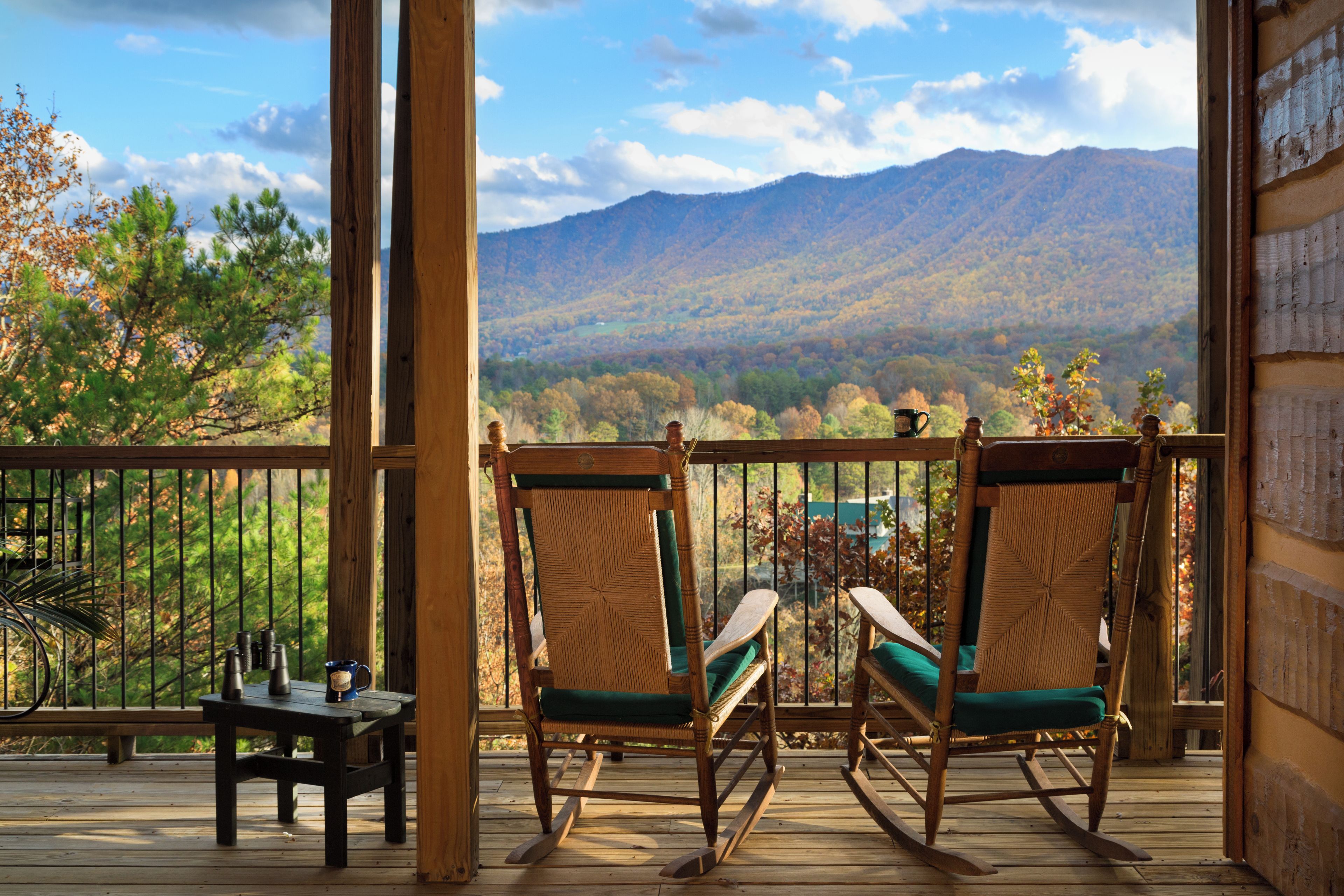 A wooden deck with two rocking chairs facing a mountainous landscape.