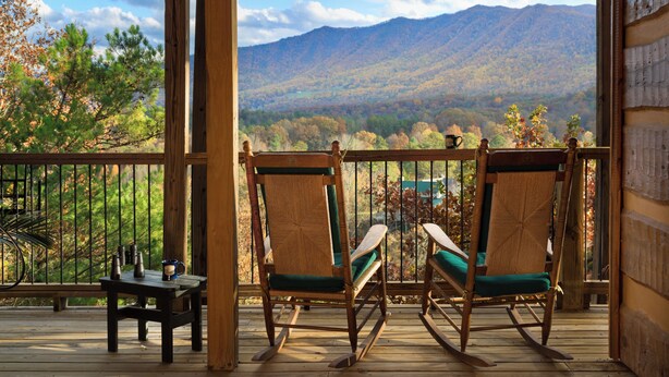 A wooden deck with two rocking chairs facing a mountainous landscape.