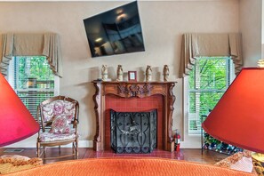 Una habitación con chimenea, un televisor montado en la pared y una silla con cojín estampado.