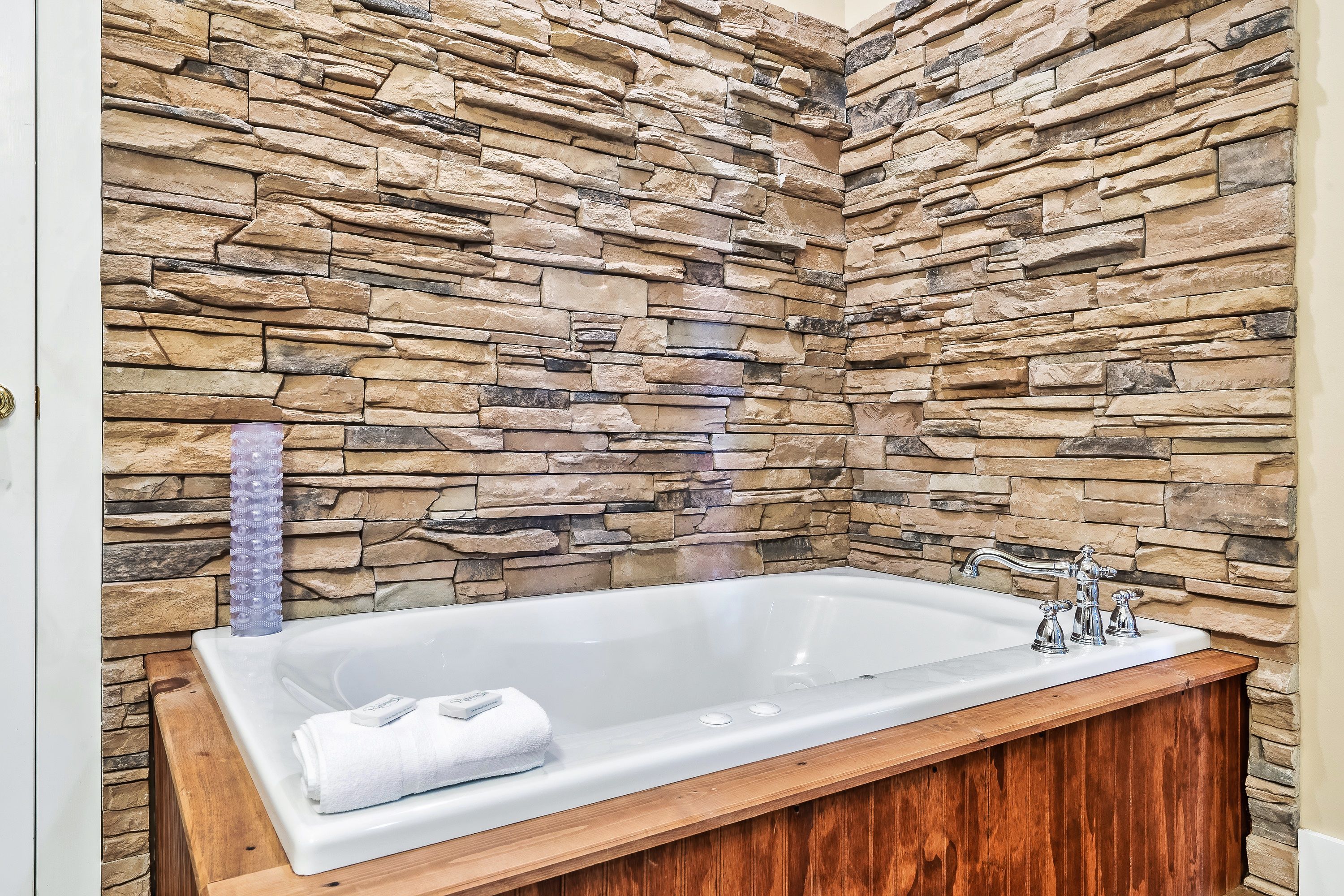 A stone wall bathroom with a white bathtub, wooden vanity, and a towel.
