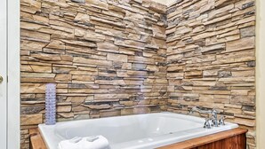A stone wall bathroom with a white bathtub, wooden vanity, and a towel.