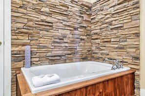 Un bagno con parete in pietra, vasca da bagno bianca e mobile lavabo in legno.