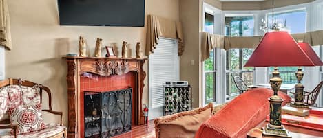 Una sala de estar con chimenea, un televisor montado en la pared y un sillón rojo.