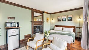 Ein Hotelzimmer mit Bett, zwei Sesseln, einer Kaffeebar, einem Kamin und Kunstwerken an den Wänden.