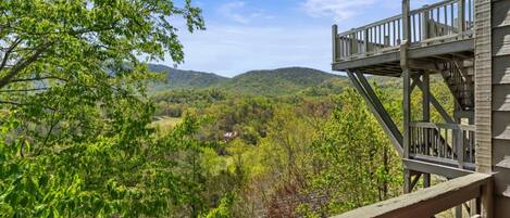 A wooden deck with a view of a forested valley and distant mountains.