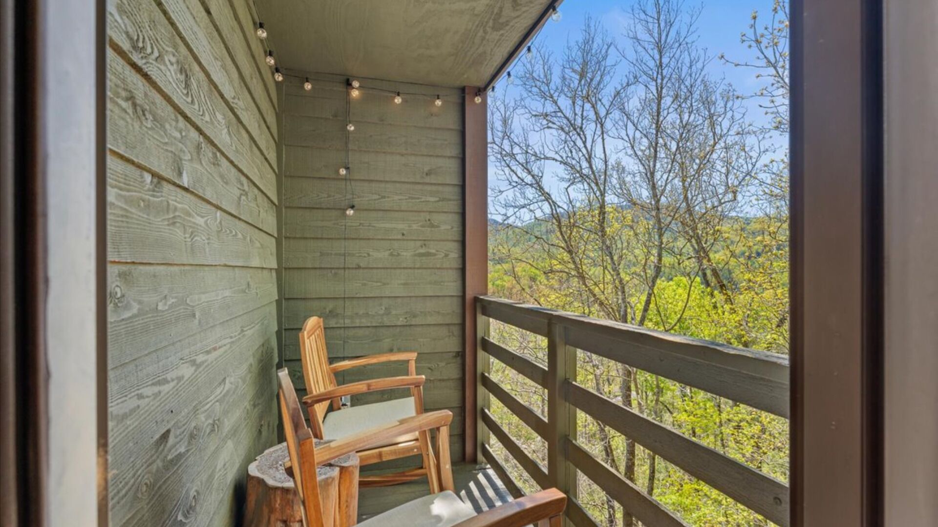 A wooden balcony with a wooden chair and a bench, overlooking a forested area.