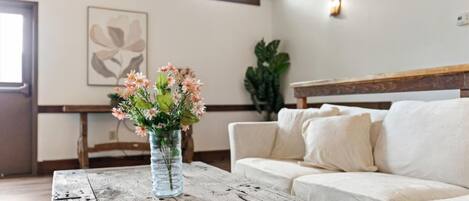 A living room with a wooden coffee table, a white sofa, and a vase of flowers.