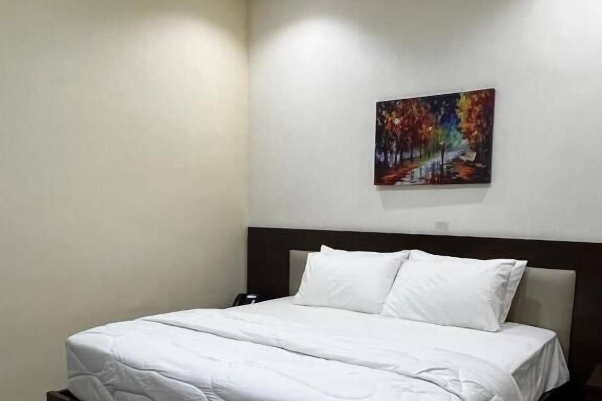 A modern bedroom with a large bed, a headboard, a nightstand, and a painting on the wall.
