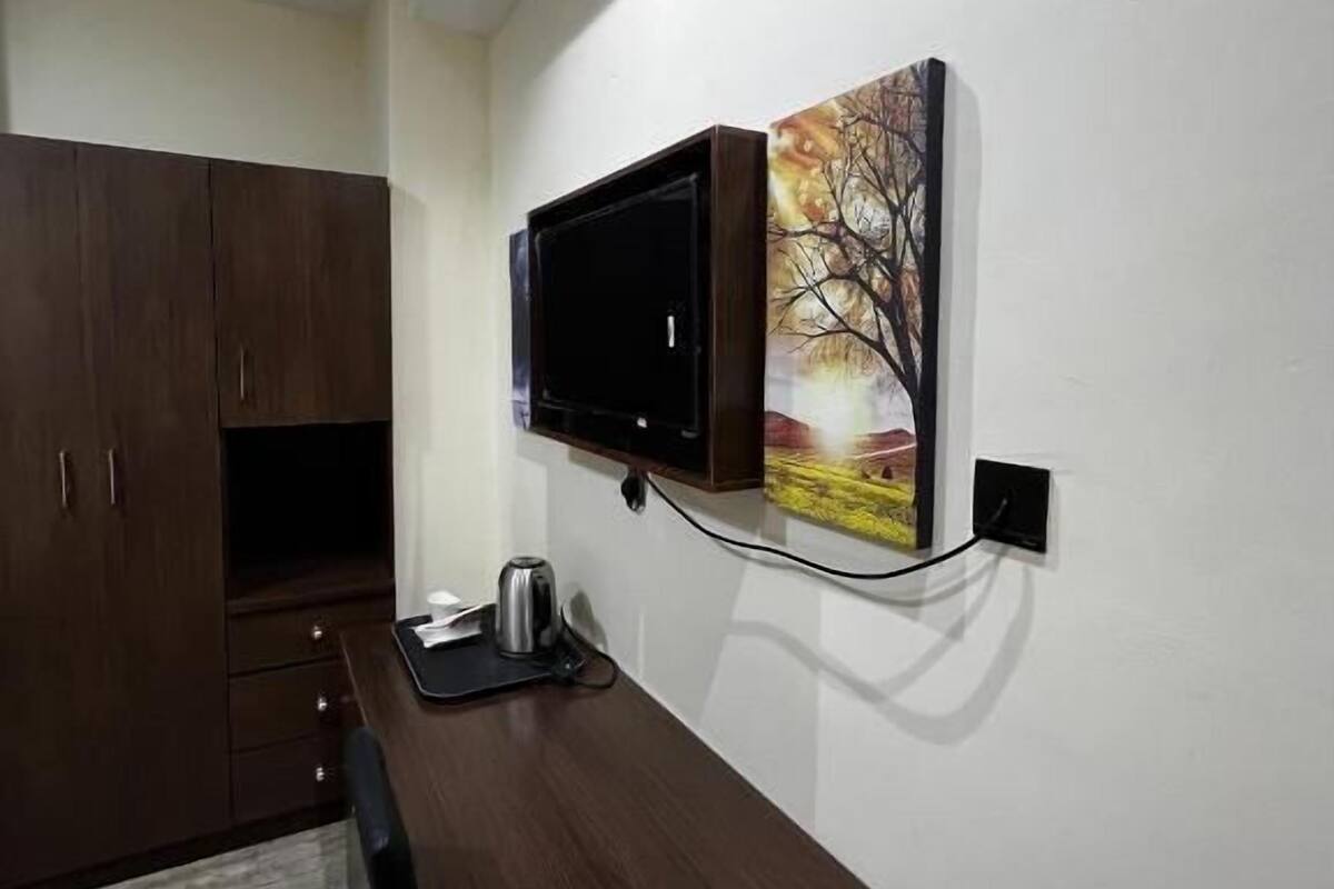 A compact room with a wooden desk, a mounted TV, and a painting on the wall.