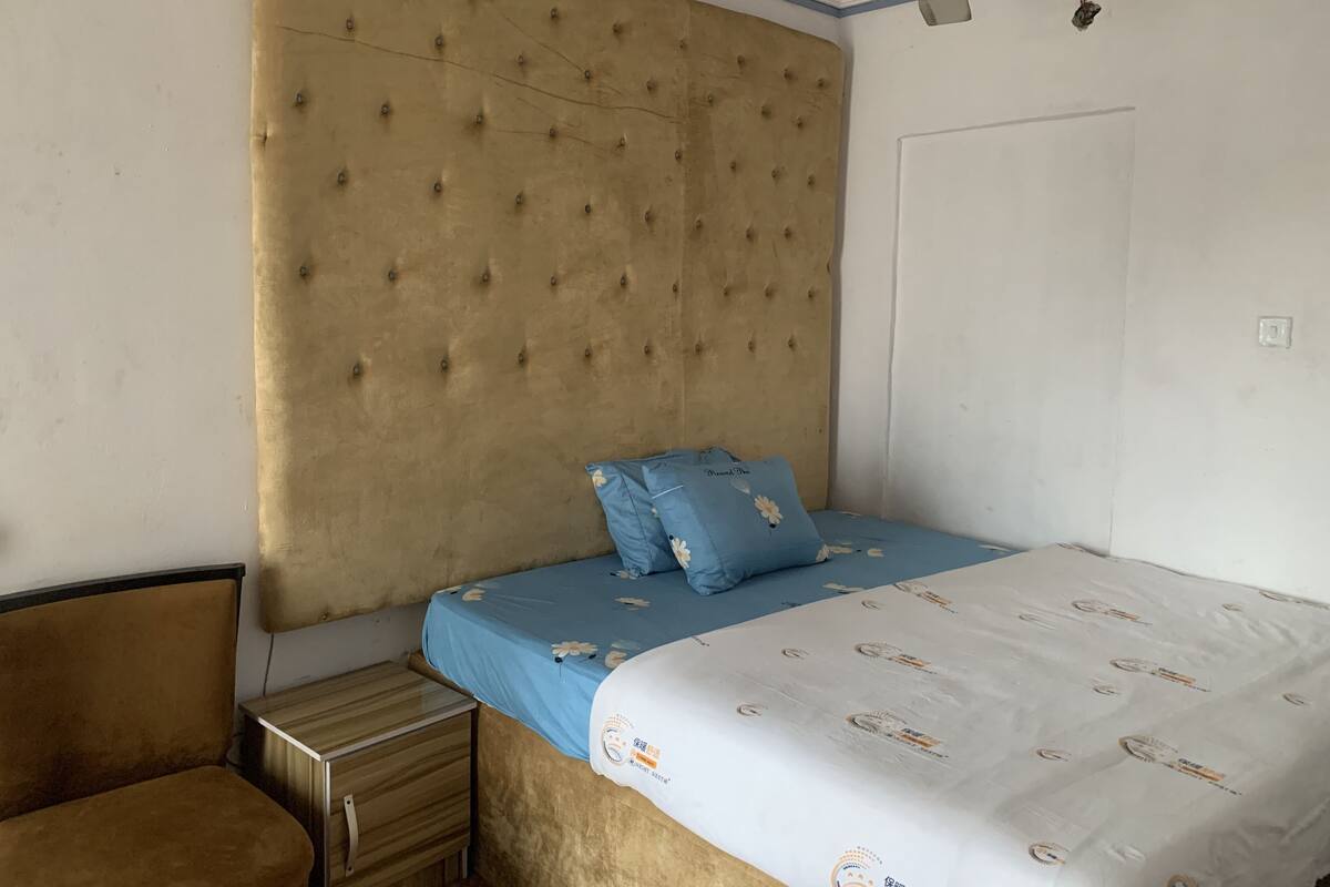 A bedroom with a tufted headboard, a bed with a blue floral bedspread, a blue pillow, and a wooden nightstand.