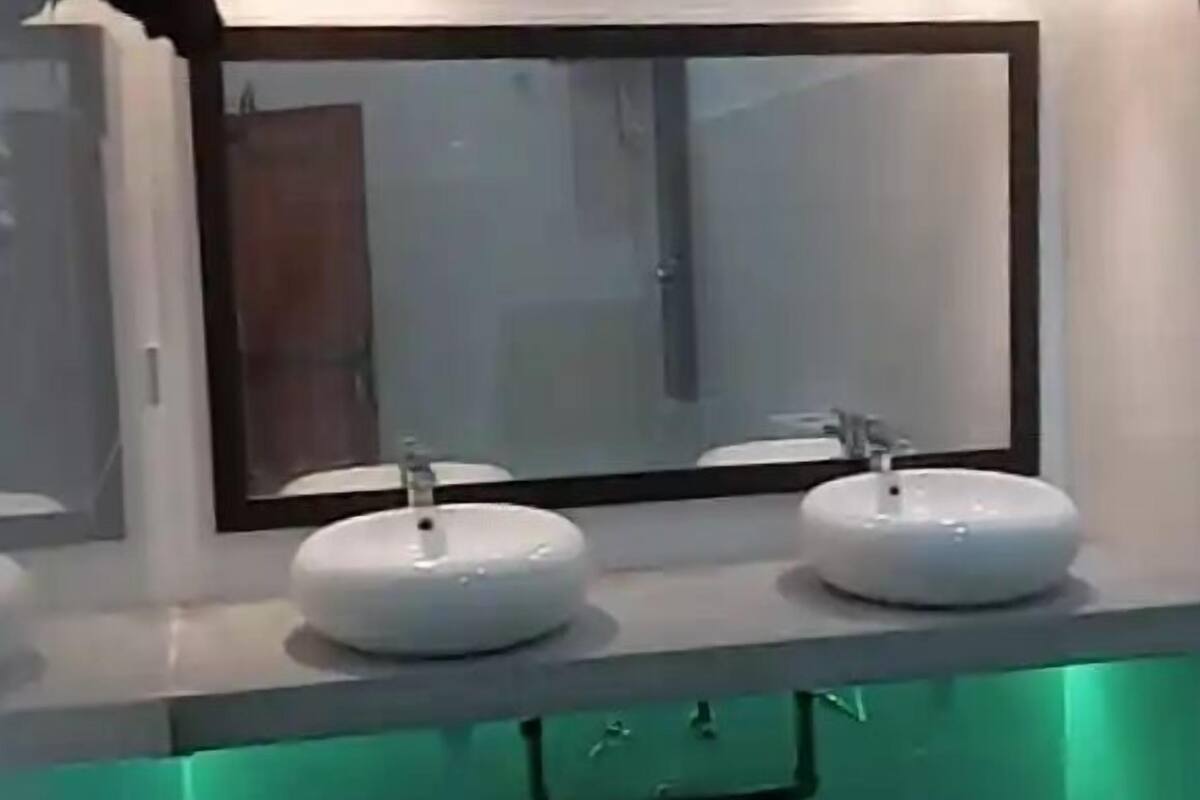 A bathroom with two white sinks, a mirror above, and a green-lit under-counter area.